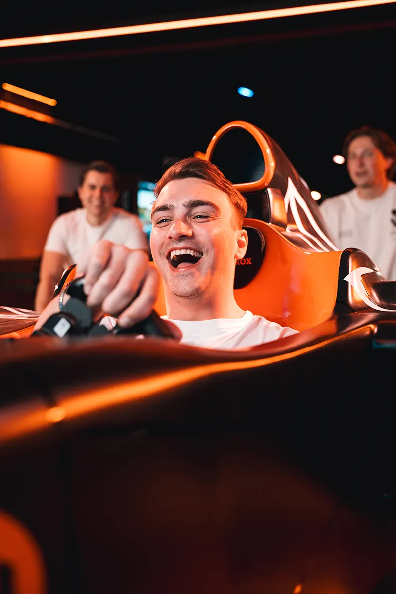 Lachende man in oranje F1 race cockpit bij PlayRena